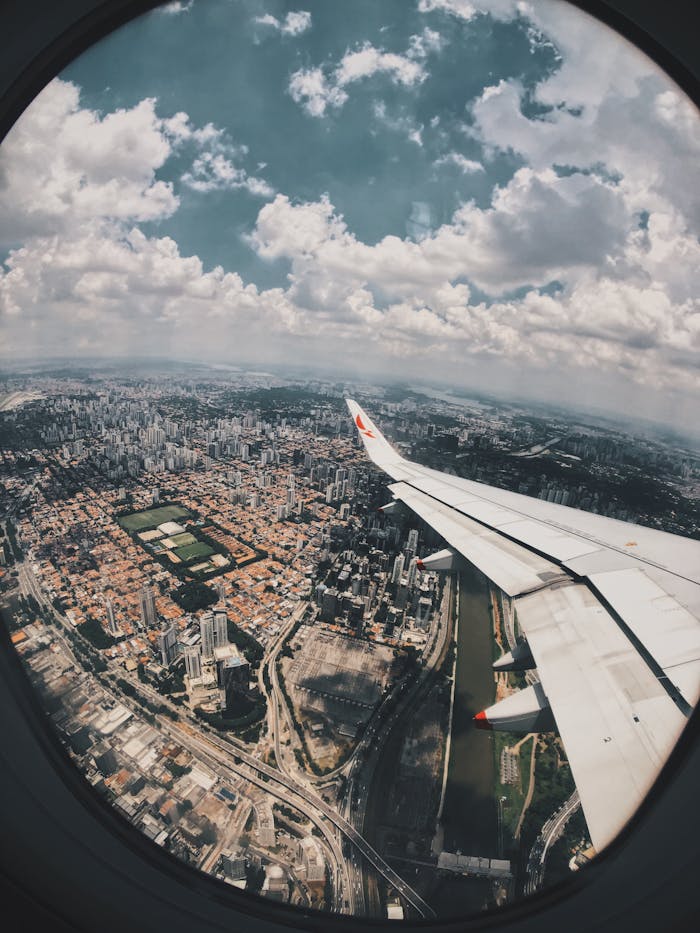 Aerial cityscape captured from airplane window with skyline and clouds, showcasing travel and transportation.